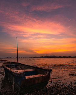 Boat moored on beach against sky during sunset