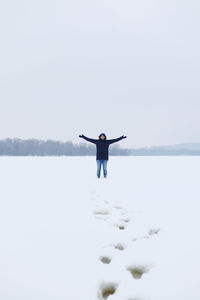 Full length of man with arms outstretched standing on snowy field against clear sky