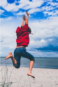 Full length of woman jumping at beach against sky