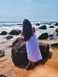 Rear view of woman on rock at beach against sky