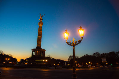 Victory column and illuminated street light against sky at night