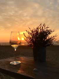 Wine glass on table by sea against sky during sunset