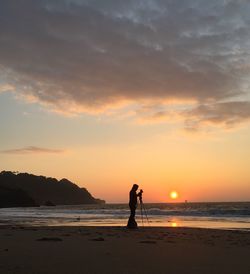 Silhouette man photographing at beach against sky during sunset