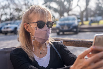 Mature adult woman smiling with glasses wearing face mask looking at smartphone.