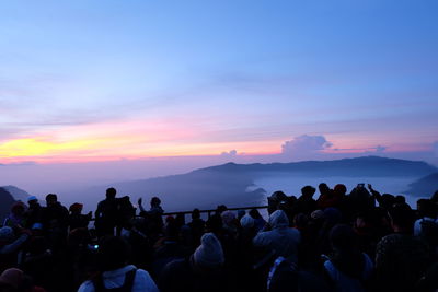 Group of people on mountain against sky during sunset