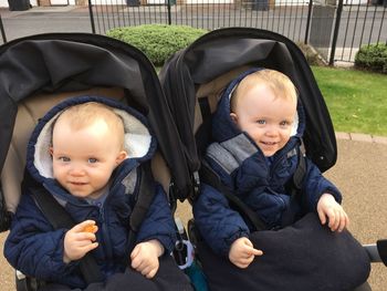 Portrait of smiling twin brothers sitting in baby carriage at footpath