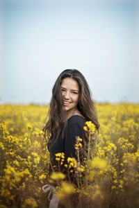 Young woman smiling on field against yellow sky
