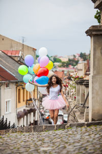 Full length of happy woman with balloons standing against building