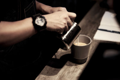 Midsection of man pouring milk in coffee cup