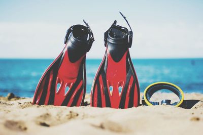 Close-up of diving flippers on sand at beach against sky