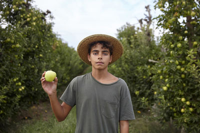 A boy with an apple in the middle of an apple field