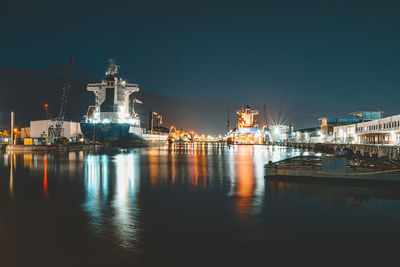 Illuminated harbor by sea against sky at night