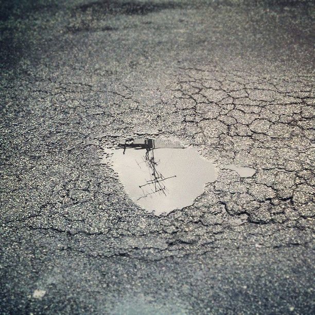 high angle view, street, transportation, puddle, road, asphalt, water, day, nature, outdoors, tranquility, no people, reflection, textured, wet, sunlight, fuel and power generation, cracked, tranquil scene, dry