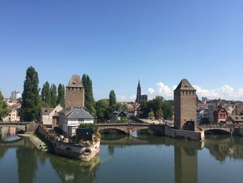 Buildings by river against clear blue sky