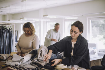 Young female fashion designer examining clothes while working at workshop