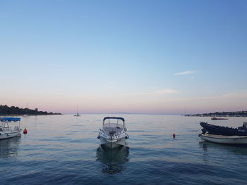 Sailboats moored in sea against sky during sunset