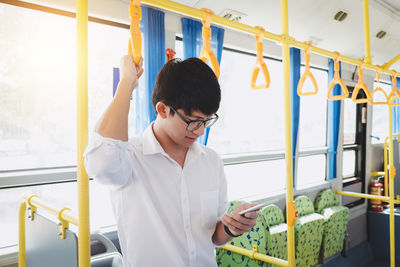 Young man using mobile phone while standing in train