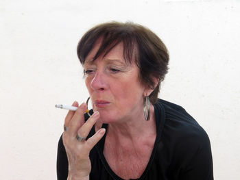 Woman smoking while sitting against wall