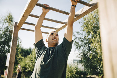 Male athlete hanging on monkey bar in park on sunny day