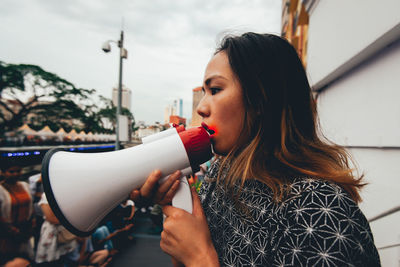 Woman holding megaphone while looking away against sky