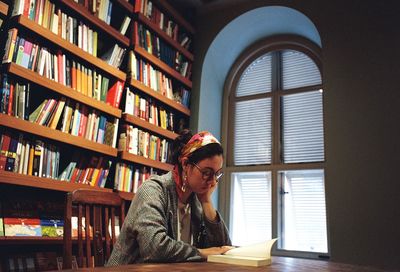Woman reading book while sitting at table in library