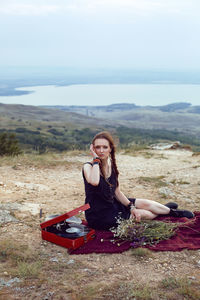 Young woman lies in nature in a black dress next to an old gramophone and listens to music