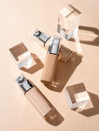 Foundation beauty product is glass bottle with glass cubes and prisms, hard shadows