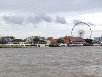 Ferris wheel by sea against buildings