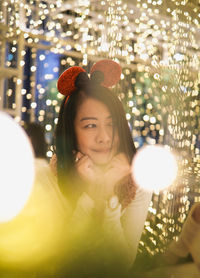 Portrait of young woman standing against illuminated christmas tree