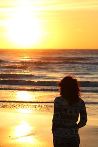 Rear view of woman standing at beach during sunset