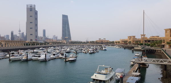 Boats moored in river by buildings against clear sky