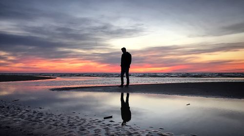 Silhouette man standing on beach against sky during sunset