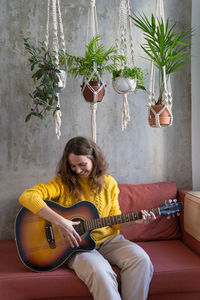 Woman playing guitar while sitting on sofa