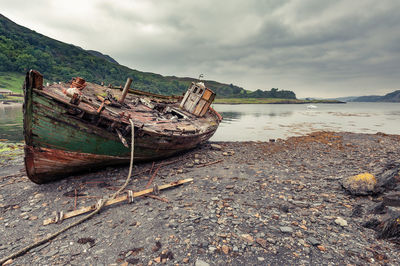 Abandoned boat moored on beach against sky