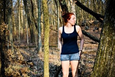 Young woman standing against trees at forest