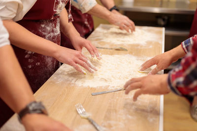 The hands of several people are kneading the dough on the table. mix a raw egg with flour.