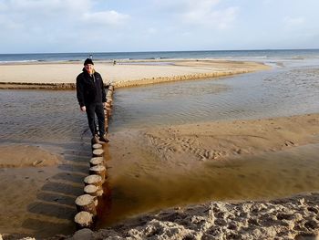 Man standing on wooden post against sea at beach