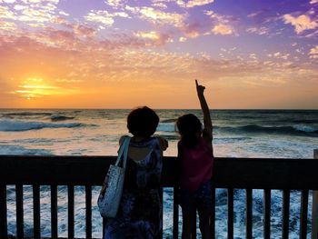 People standing by railing against sea during sunset