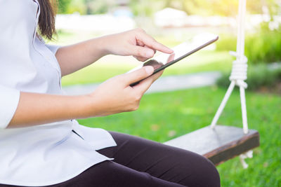 Midsection of woman using digital tablet while sitting on swing at park