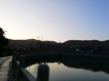 Reflection of silhouette trees in water against clear sky