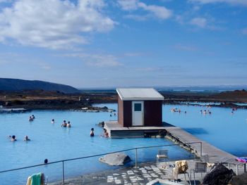 People in swimming pool by lake against sky