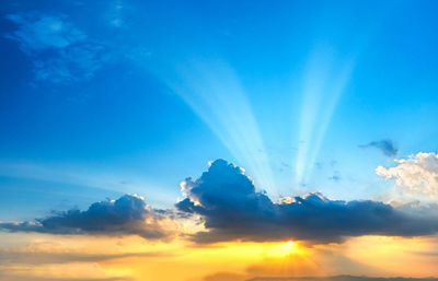 Low angle view of sunlight streaming through clouds during sunset