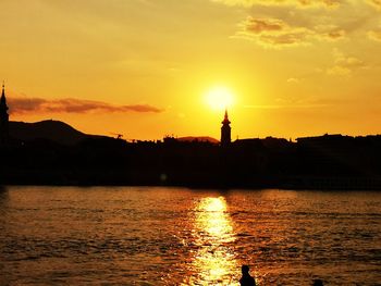 Silhouette lighthouse by sea against orange sky