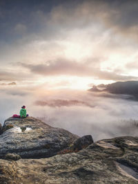 Alone travel woman hiker sits on edge of cliff and enjoying sunrise looking at valley and mountains