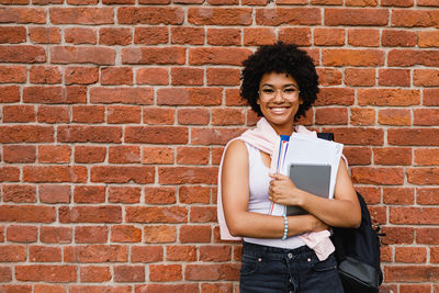 Portrait of a smiling young woman standing against brick wall