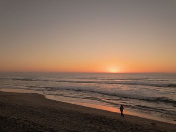 High angle view of man walking on shore at beach against sky during sunset