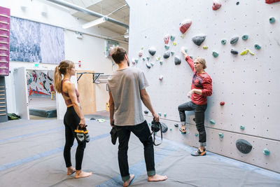 Mature trainer training male and female students for wall climbing in gym