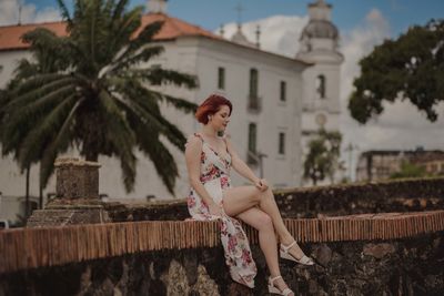 Woman sitting on retaining wall against building