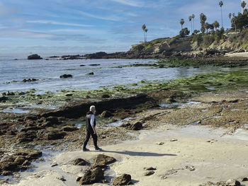 Woman standing on rock at beach against sky