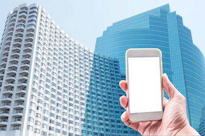 Midsection of person holding mobile phone against modern building